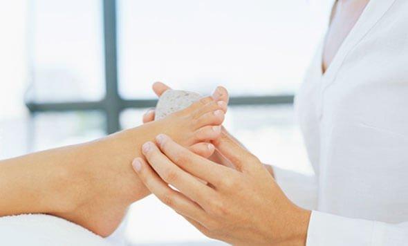 एक प्यूमिक पत्थर से फुट कॉलस को हटाती महिला